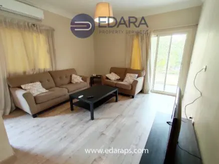 Living room featuring two beige sofas, a black coffee table, and a television stand against a light-colored wall.