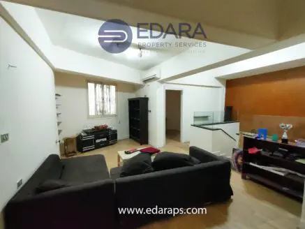 Interior view of a living space featuring a black sofa, wooden flooring, and various furniture pieces.