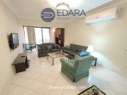 Interior view of a living room featuring a sofa set, coffee table, and television on the wall.
