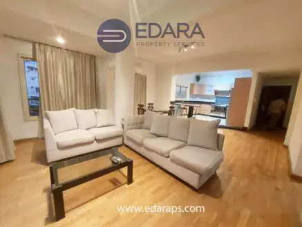 Modern living room featuring two beige sofas and a glass coffee table on wooden flooring.