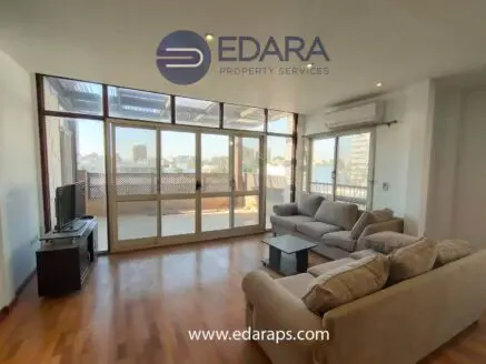 Spacious living room featuring a sofa set and large windows allowing natural light.