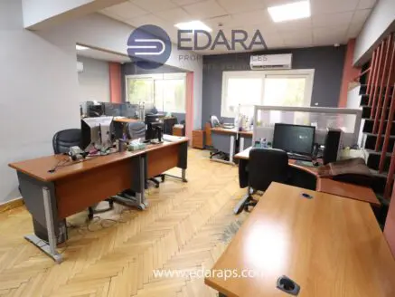 Interior view of an office workspace featuring multiple desks with computers and ergonomic chairs.