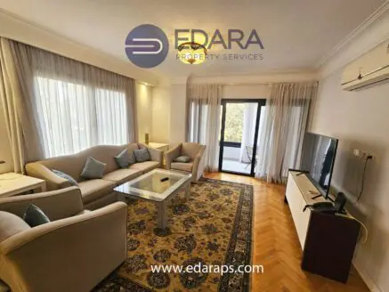Modern living room featuring a beige sofa, coffee table, and flat-screen television against a light-colored wall.