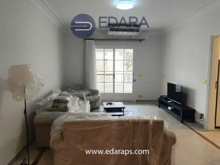 Living room featuring a sofa and armchair covered in plastic, with a television and window in the background.
