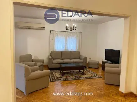 Living room featuring a beige sofa set, coffee table, and television against a white wall.