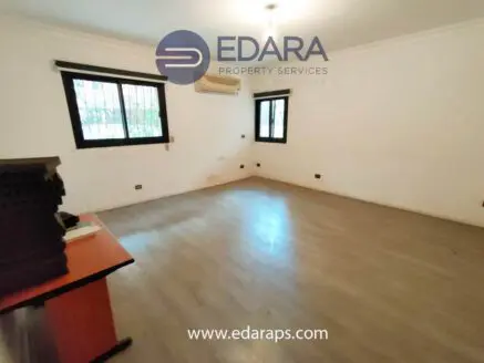 Empty room featuring a wooden floor, two windows, and a desk with stacked items in the corner.
