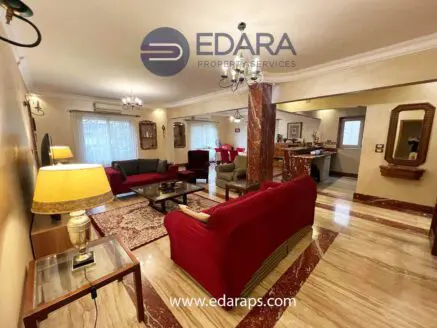 Spacious living room featuring red and beige sofas, decorative lighting, and marble flooring.