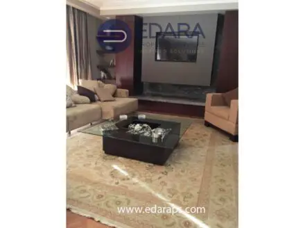 Living room featuring a beige sofa, a glass coffee table, and a decorative rug on wooden flooring.