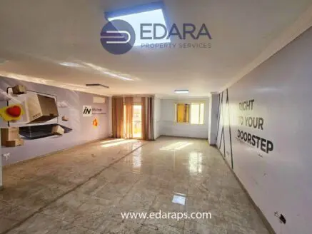 Spacious empty room with light-colored walls, large windows, and tiled flooring.