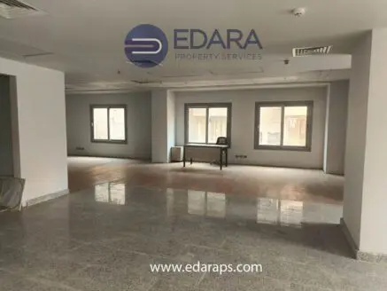 Interior view of a spacious office area featuring large windows and a light-colored floor.