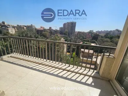 Balcony railing overlooking greenery and buildings in Cairo, with clear blue sky in the background.