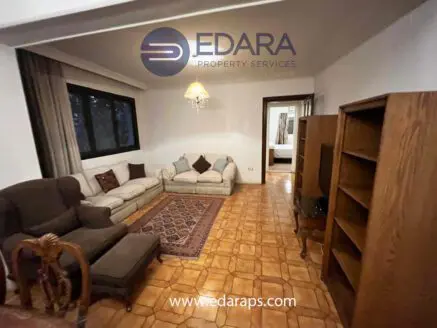 Living room featuring a light-colored sofa, dark armchair, and wooden bookshelf on tiled flooring.