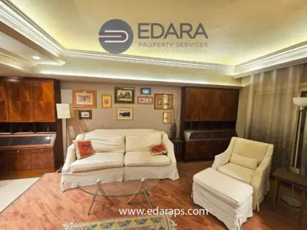 Living room featuring a white sofa, armchair, and wooden furniture against a neutral wall.