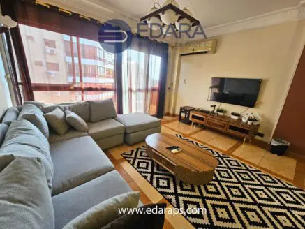 Modern living room featuring a gray sectional sofa, coffee table, and television against a backdrop of large windows.