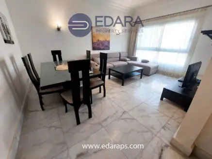 Interior view of a modern living room and dining area with a sofa, dining table, and television.