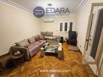 A living room featuring a beige sofa, a glass coffee table, and a television on a wooden floor.