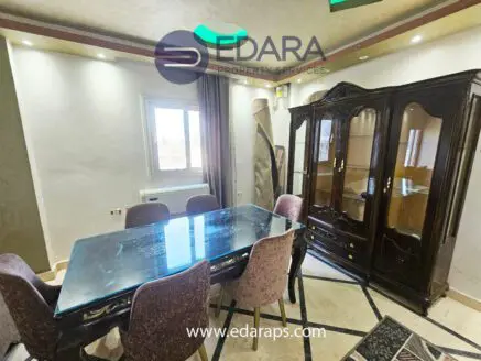 Dining room featuring a glass-top table surrounded by upholstered chairs and a wooden display cabinet.