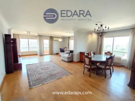 Interior view of a spacious living room featuring a dining table, chairs, and a sofa with large windows.