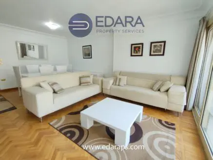Interior view of a living room featuring beige sofas and a white coffee table on a patterned rug.