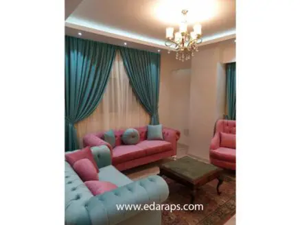 Living room featuring pink tufted sofas and blue curtains, with a wooden coffee table in the center.