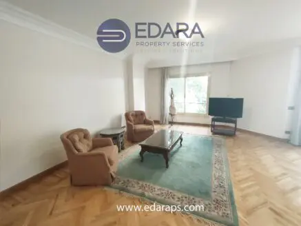 Spacious living room featuring two armchairs, a coffee table, and a television set against a light-colored wall.