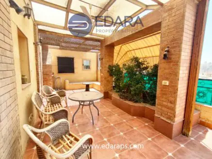 Outdoor terrace featuring a round table and wicker chairs surrounded by greenery in a residential setting.
