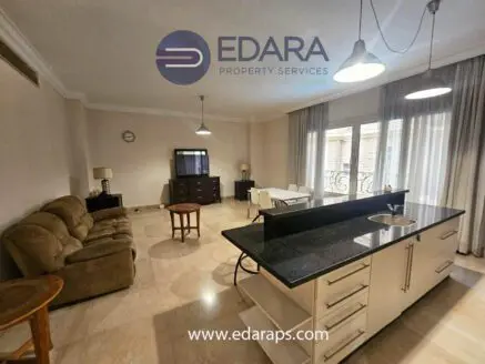 Interior view of a modern living room and kitchen area with a sofa, table, and cabinets.