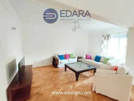 Bright living room featuring a white sofa set with colorful cushions and a glass coffee table.