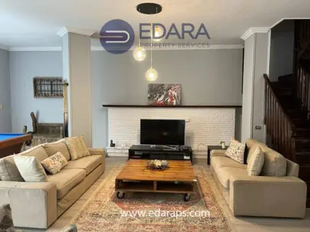Living room featuring a beige sofa set, wooden coffee table, and a television on a white brick wall.