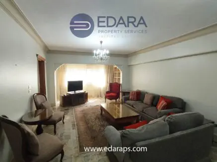 Living room featuring a gray sofa set, coffee table, and a television against a light-colored wall.