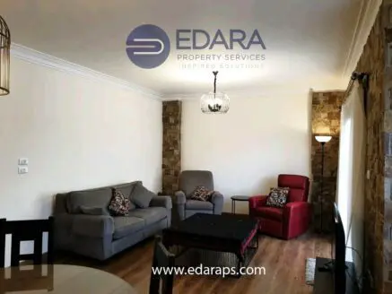 Living room featuring a gray sofa, red armchair, and wooden flooring with decorative elements.