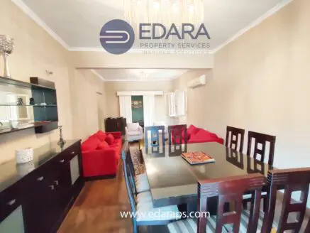 Dining table with chairs in a modern interior featuring a chandelier and red sofas.