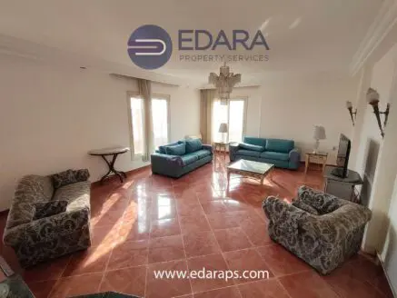 Spacious living room featuring blue and gray sofas with a marble coffee table and large windows.