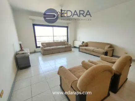 Spacious living room featuring beige sofas and a large window with natural light.