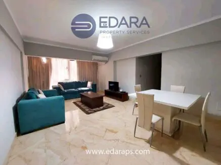 Interior view of a modern living room with a teal sofa and dining table in a well-lit space.