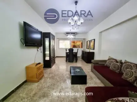 Living room featuring a red sofa, television mounted on the wall, and a dining table with chairs.
