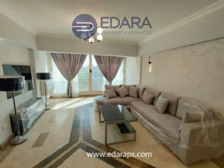 Living room featuring a light-colored sofa, coffee table, and large windows with curtains.