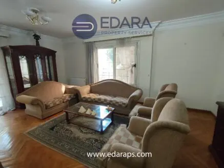 A living room featuring a beige sofa set, glass coffee table, and decorative rug in a well-lit space.