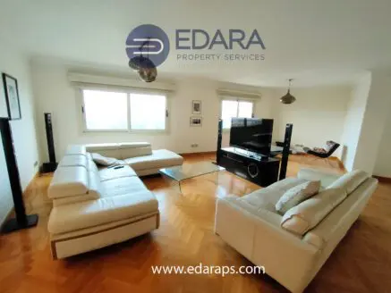 Spacious living room featuring a white leather sofa set and a television on a glass stand.