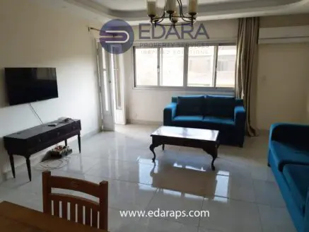 Living room featuring two blue sofas, a wooden coffee table, and a television mounted on the wall.