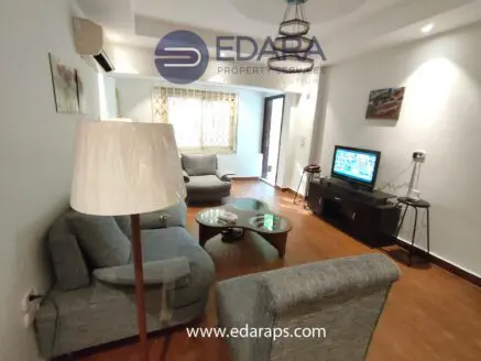 Living room featuring gray sofas, a coffee table, and a television set against a light-colored wall.