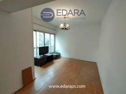 Living room space with a television on a stand, featuring a chandelier and wooden flooring.
