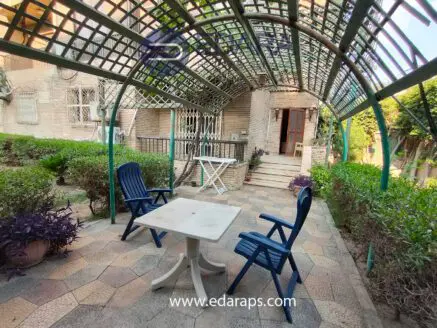 Outdoor seating area featuring a table and two blue chairs under a trellis structure.