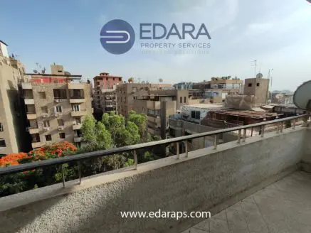 View from a balcony overlooking residential buildings in Cairo with greenery and rooftops visible.