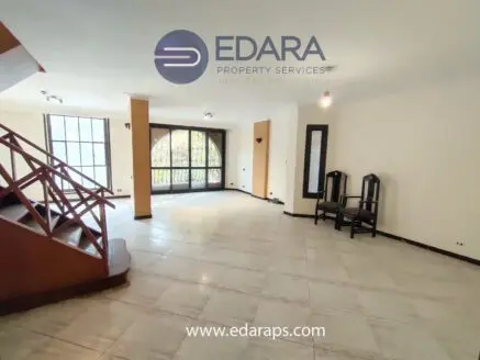 Bright living room featuring large windows and a staircase, with two chairs positioned against the wall.