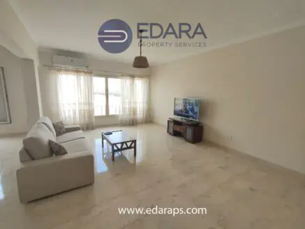 Bright living room featuring a beige sofa, wooden coffee table, and a television on a stand.