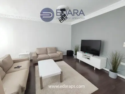 Living room featuring a beige sofa set, a white coffee table, and a television on a stand against a gray wall.
