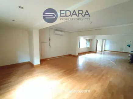 Interior view of a spacious, unfurnished room with wooden flooring and air conditioning unit on the wall.