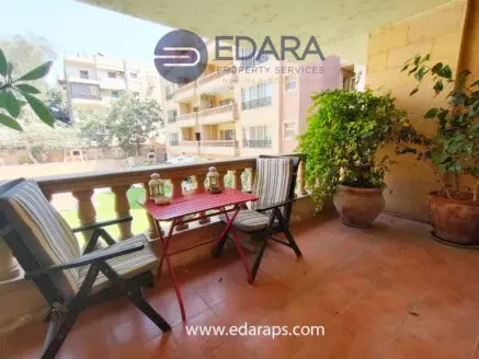 Seating area on a balcony with two chairs and a small table, surrounded by potted plants.