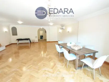 Bright living room featuring a wooden dining table and chairs, with polished wooden flooring and neutral wall colors.